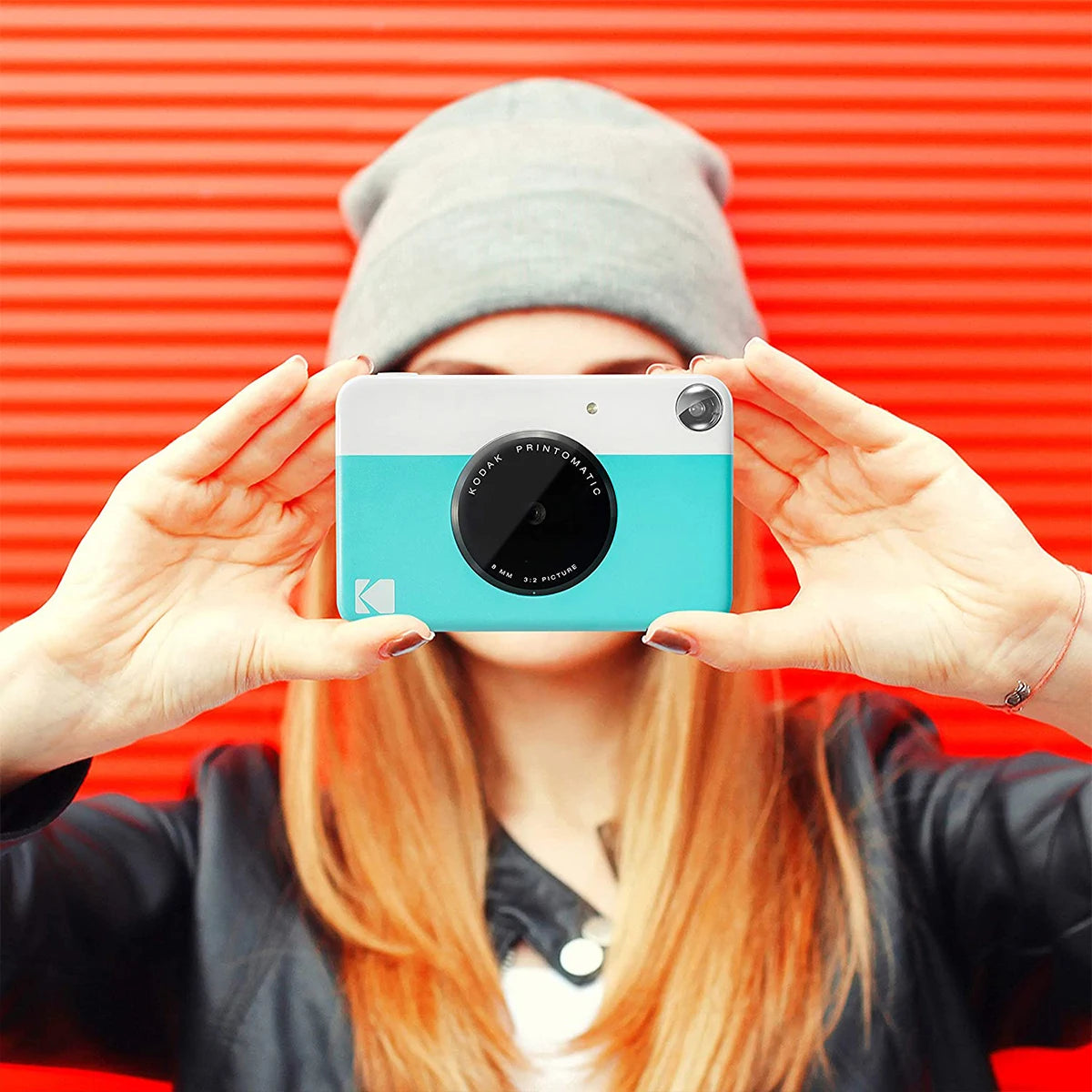 Person holding a turquoise camera against an orange background
